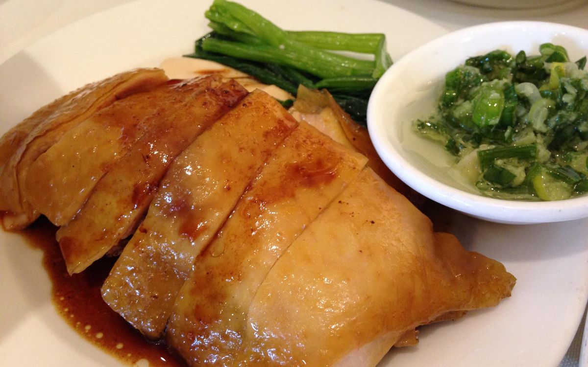 Sliced Cantonese soy sauce chicken on a plate with gai lan and a dish of ginger-scallion relish