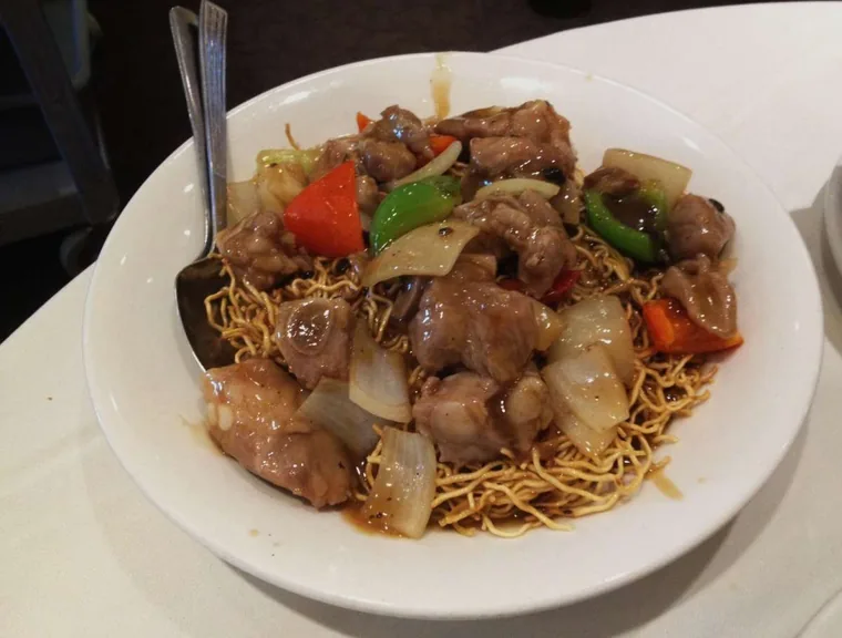 Bowl of beef with green and red peppers and onion in black bean sauce over crispy pan-fried noodles