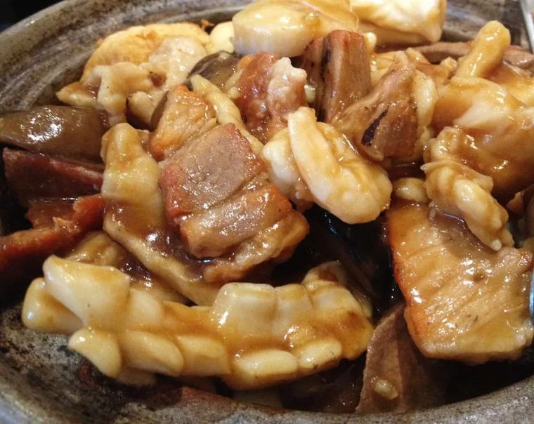 Close-up of braised pork belly, squid, mushrooms and tofu in glossy brown sauce inside a clay pot