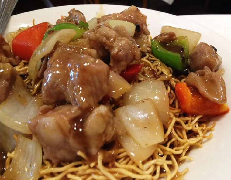 Close-up of beef with onion, green pepper and black beans piled on crispy fried noodles