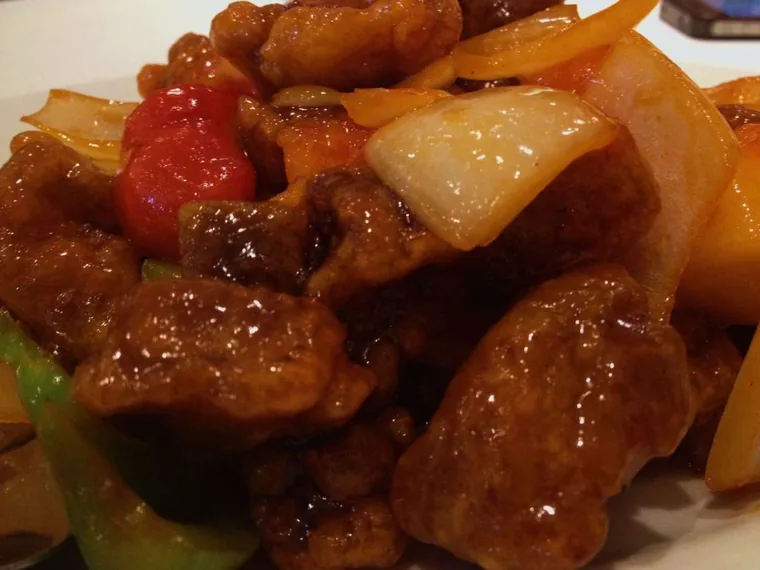 Close-up of sweet and sour pork pieces with onion, green pepper and a glossy red glaze