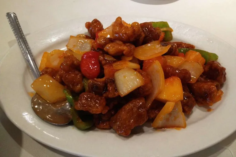 Plate of sweet and sour pork with pineapple, onion and green pepper in a glossy red sauce